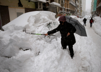 A woman tries to remove the snow from her car during a heavy snowfall in downtown Madrid, Spain, Saturday, Jan. 9, 2021. A persistent blizzard has blanketed large parts of Spain with 50-year record levels of snow, halting traffic and leaving thousands trapped in cars or in train stations and airports that suspended all services as the snow kept falling on Saturday. (AP Photo/Andrea Comas)