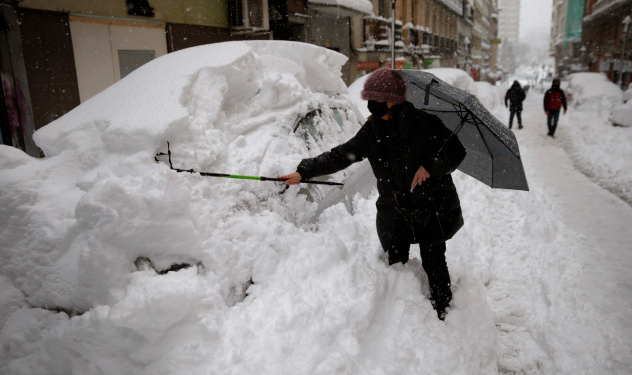 A woman tries to remove the snow from her car during a heavy snowfall in downtown Madrid, Spain, Saturday, Jan. 9, 2021. A persistent blizzard has blanketed large parts of Spain with 50-year record levels of snow, halting traffic and leaving thousands trapped in cars or in train stations and airports that suspended all services as the snow kept falling on Saturday. (AP Photo/Andrea Comas)